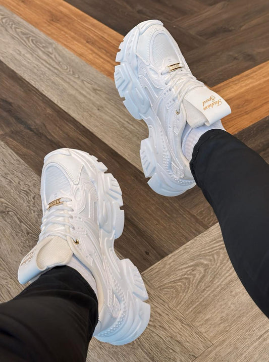 White chunky platform sneakers worn with black pants on wood floor women's stylish platform shoes for casual streetwear